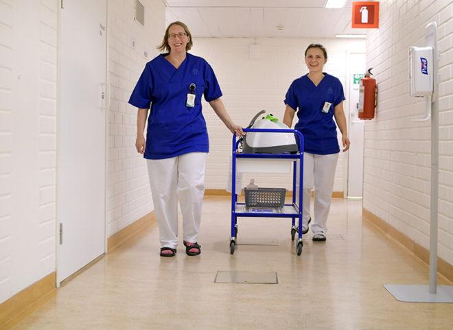 Alexandra Capatina ja hänen esimiehensä Carina Salin työntävät kärryä, jossa on desinfiointilaite.