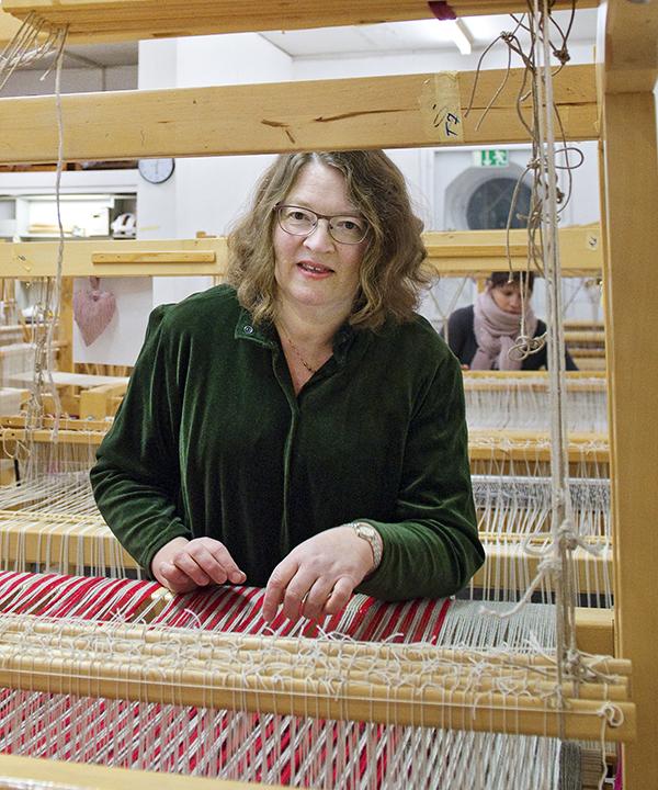 Solveig Stenroos kangaspuiden äärellä. Kangaspuilla on puna-valkoinen loimi.
