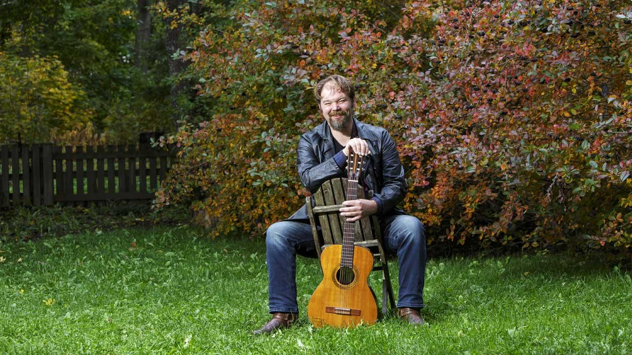 Fredrik Olkinuora istuu tuolilla puutarhassa kitaransa kanssa.