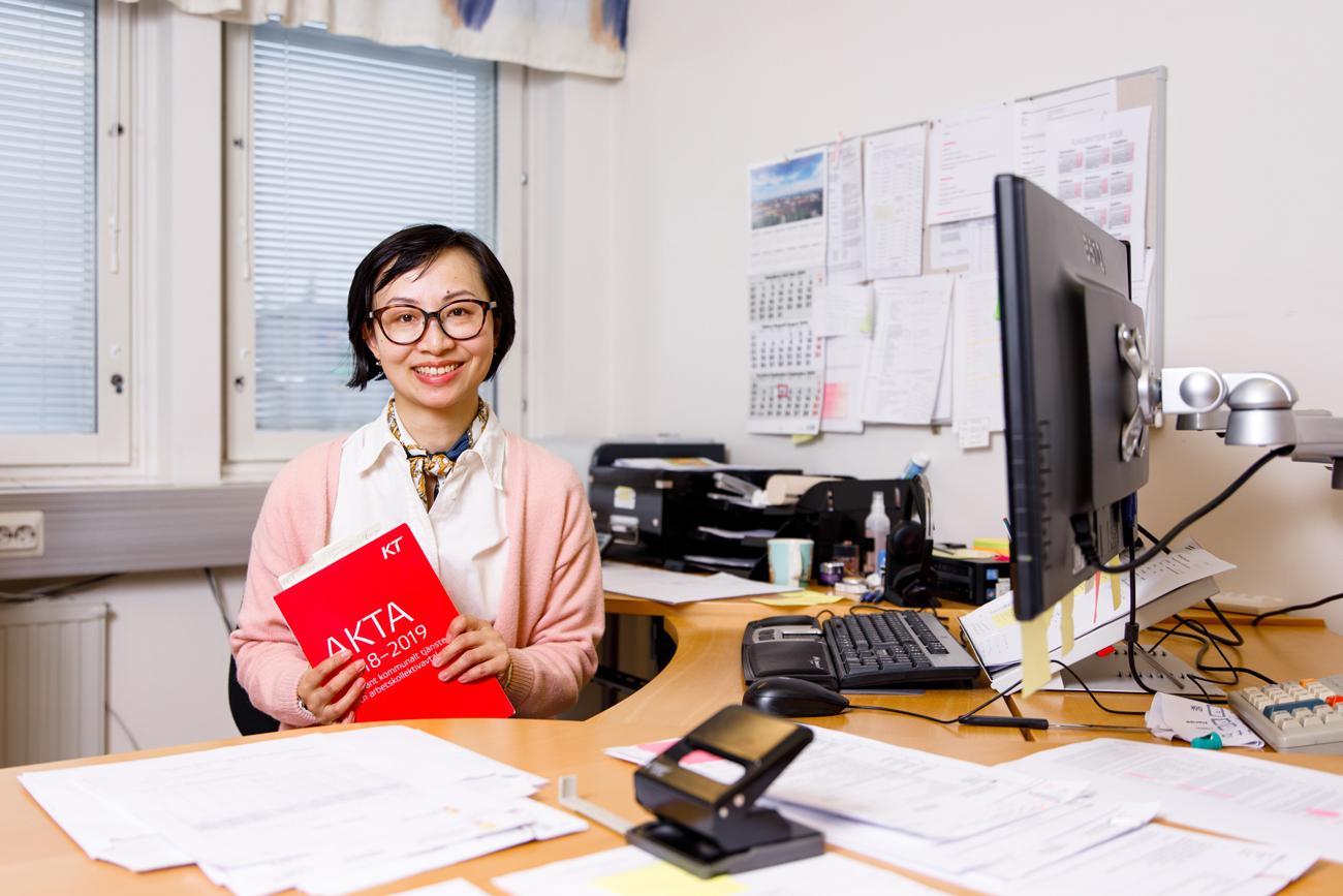 Jing Li sitter vid skrivbordet med kollektivavtalet AKTA i handen.