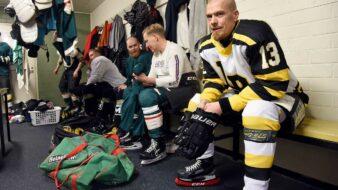 Los Bombers-spelaren Tony Hästbacka sitter i sin ishockeyutrustning på bänken i omklädningsrummet med sina lagkamrater.