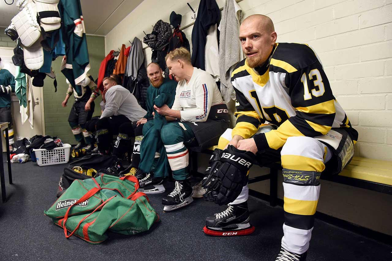 Los Bombers-spelaren Tony Hästbacka sitter i sin ishockeyutrustning på bänken i omklädningsrummet med sina lagkamrater.