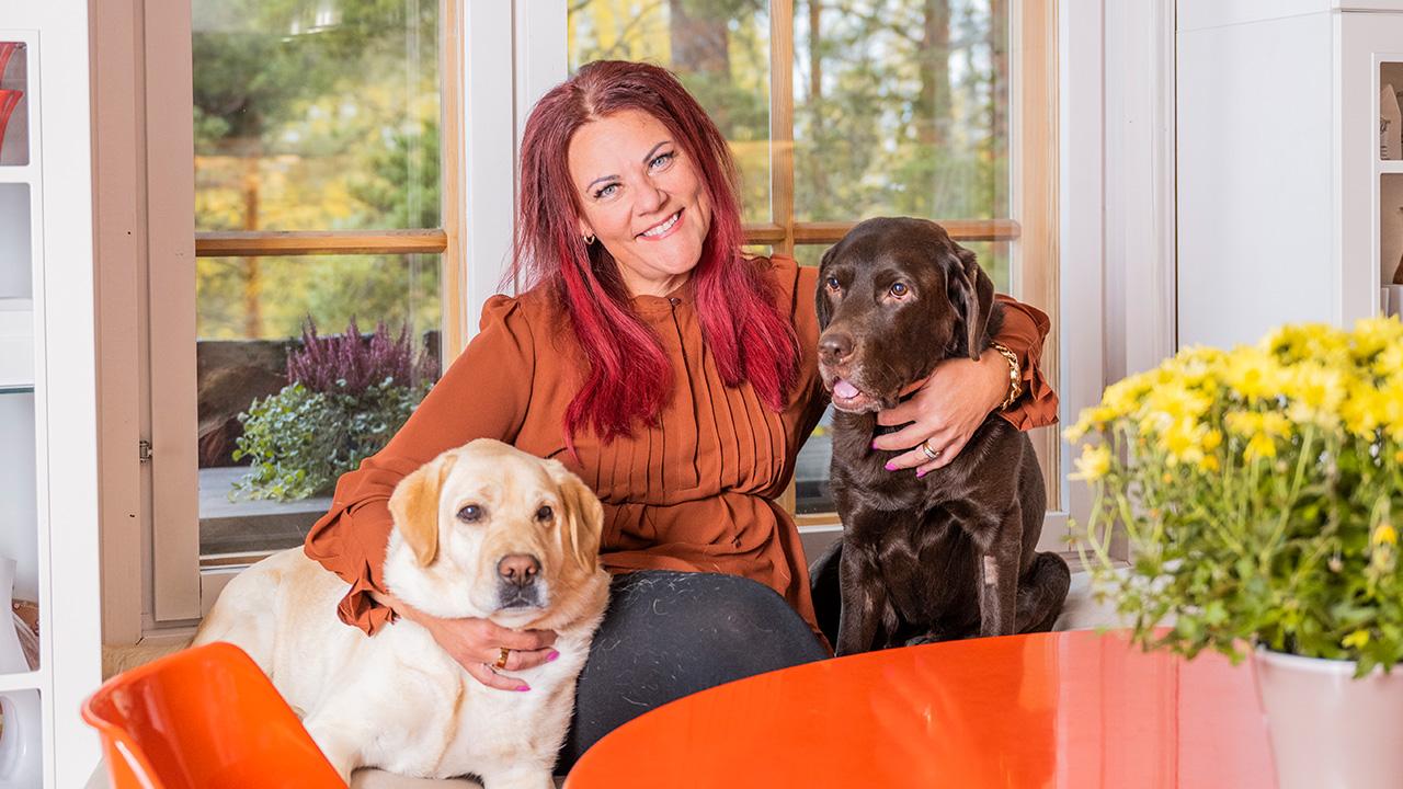 Suomen Supernanny Pia Penttala ja kaksi koiraa istuvat keittiön pöydän ääressä