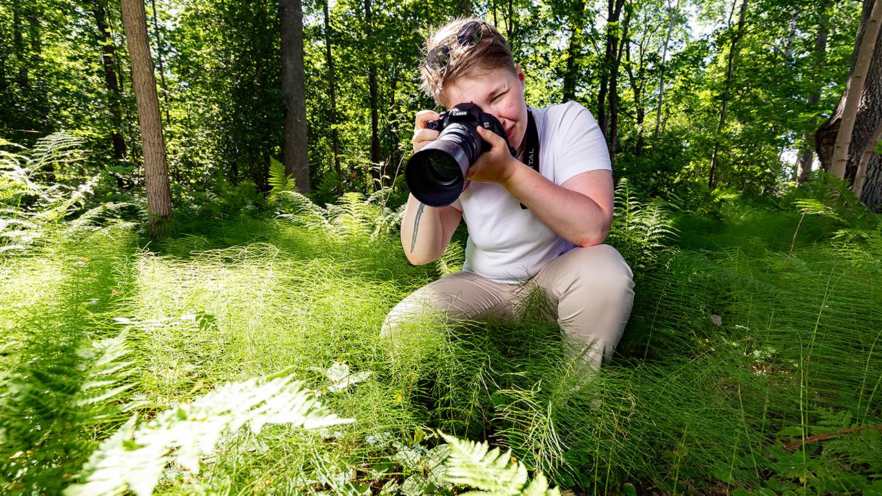 En kvinna med kameran ute på naturen.