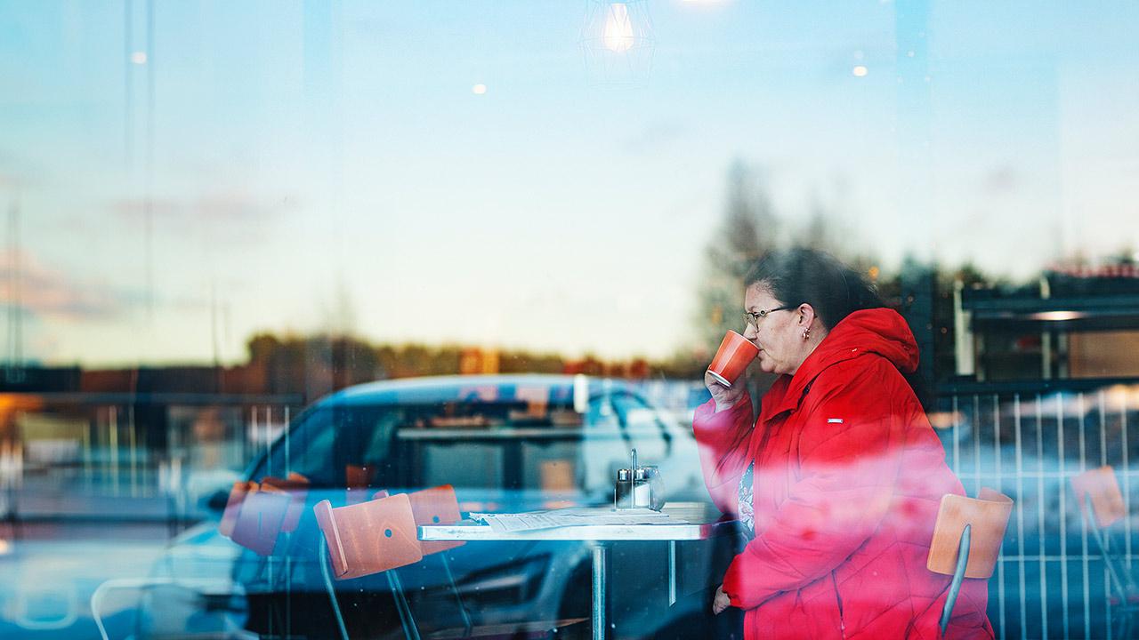 Työsuojeluvaltuutettu Päivi Virkkunen juo kahvia punaiseen takkiin pukeutuneena.
