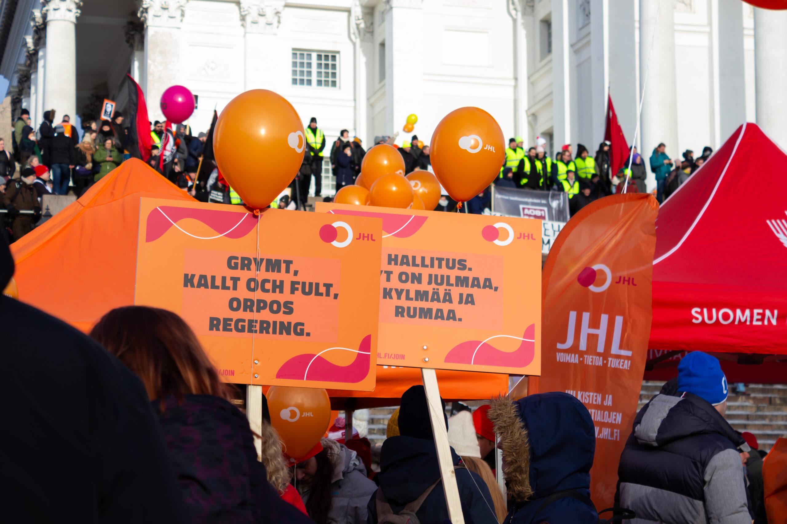 JHL-skyltar, ballonger och demonstranter framför domkyrkan på Senatstorget i Helsingfors.