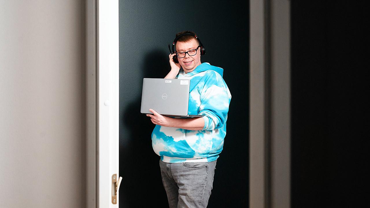 Etähoitaja Ville Ruotsalainen seisoo oven edessä, puhuu puhelua ja selaa kannettavaa tietokonetta.