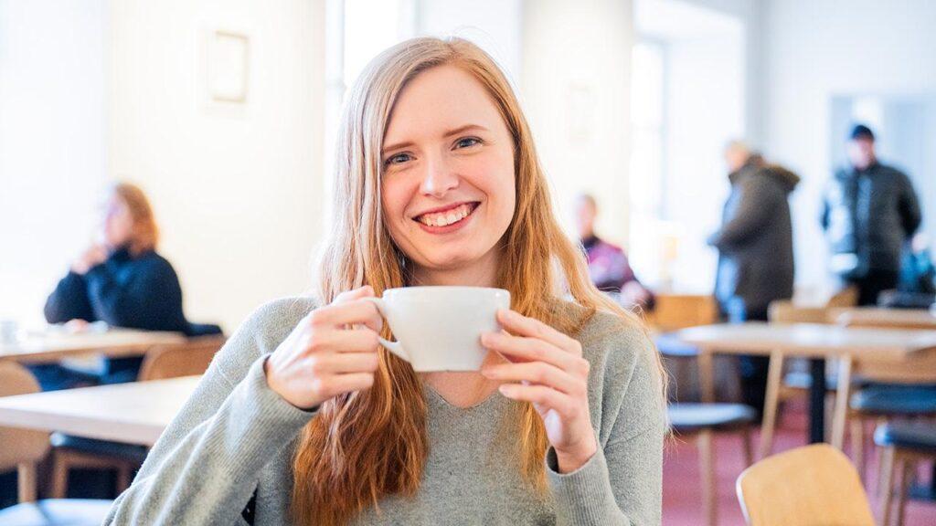 Alicia Iredale istuu kahvilassa kahvikuppi kädessään ja katsoo kameraan.