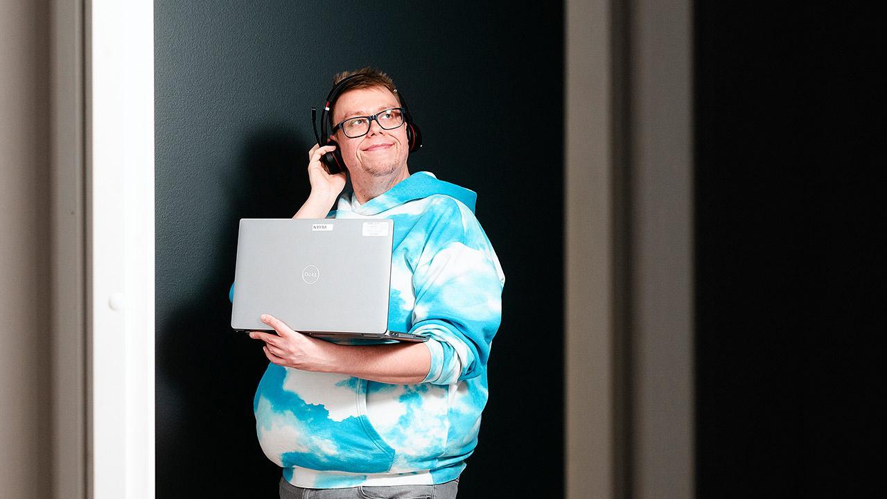 Etähoitaja Ville Ruotsalainen seisoo kannettava tietokone kädessään ja kuulokkeet päässä.