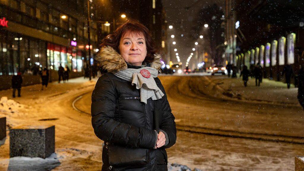 Koulunkäynninohjaaja Elvira Ansas seisoo kaupungin kadulla ja katsoo kameraan.