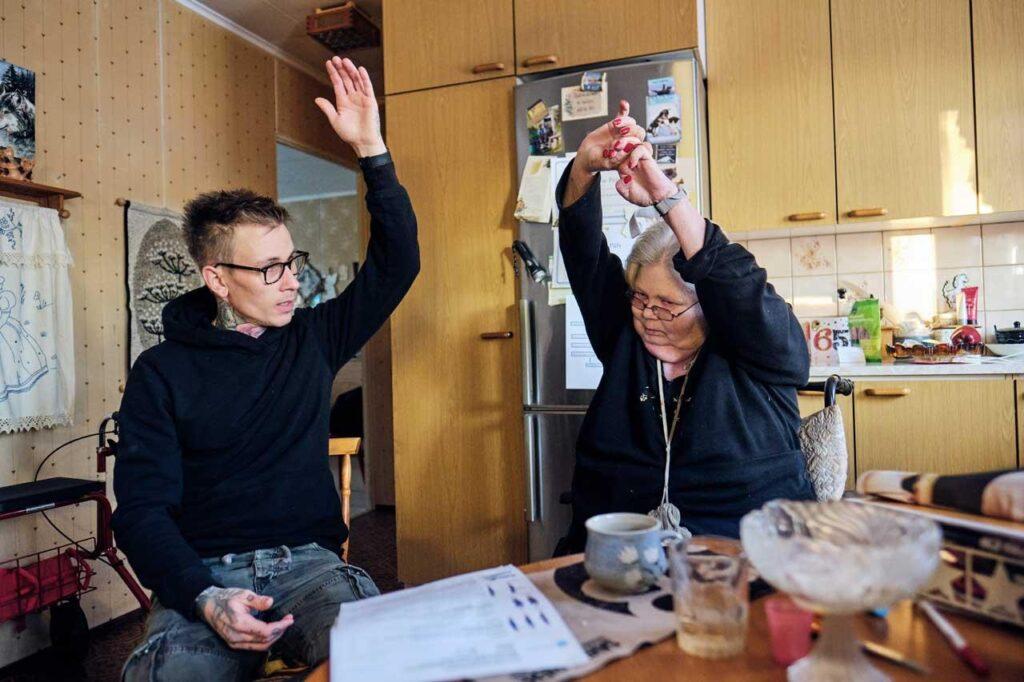 Lähihoitaja Nico Nordblad ja kuntoutettava Anne-Marie Påfs nostavat vasemmat kätensä pystyyn.