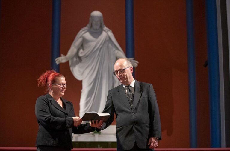 Maria och Christer Viksten läser i psalmboken framför Kristusstatyn i Lovisa kyrka.