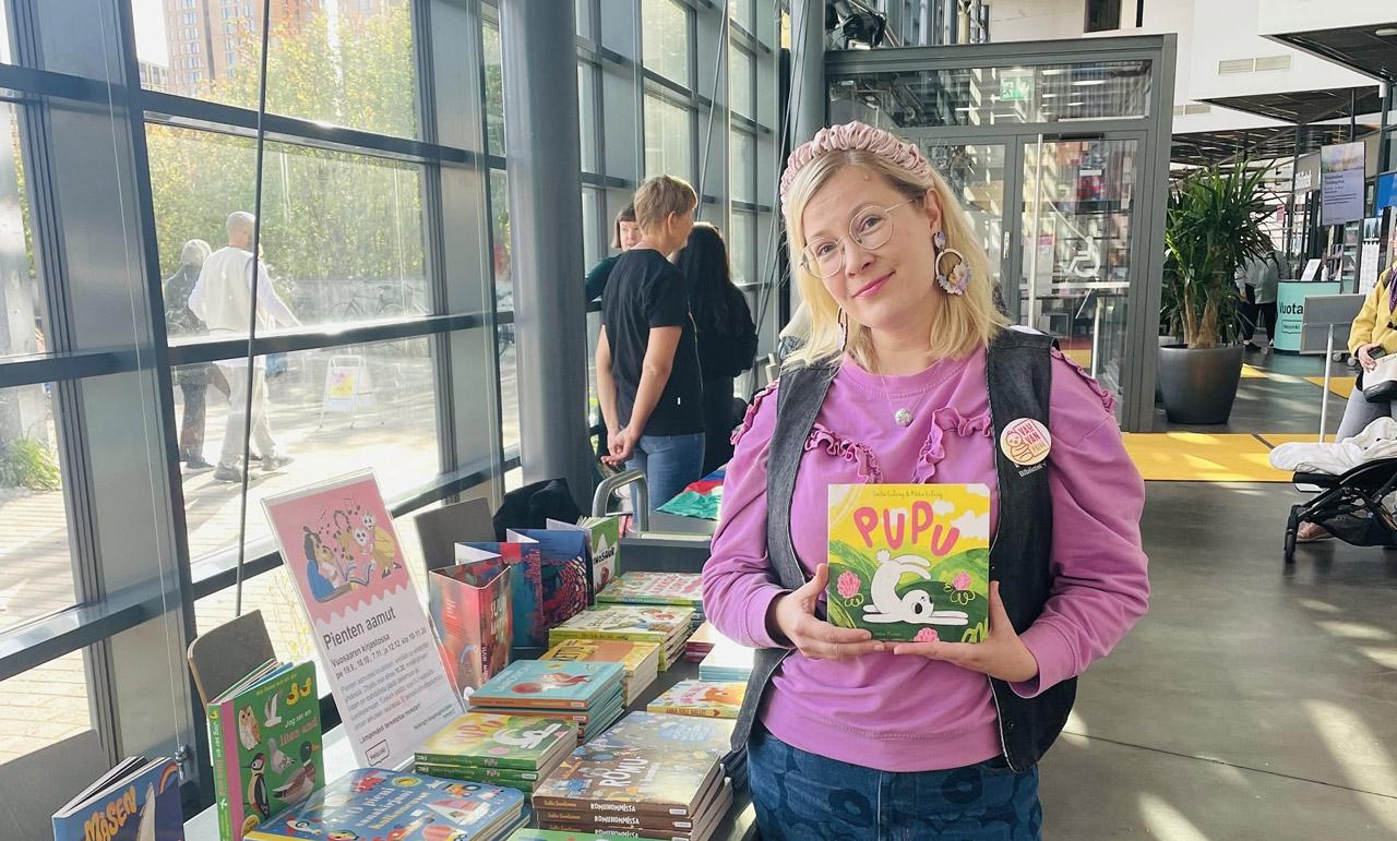 Kirjastotyöntekijä Emilia Kämäräinen hymyilee kirjastosalissa.