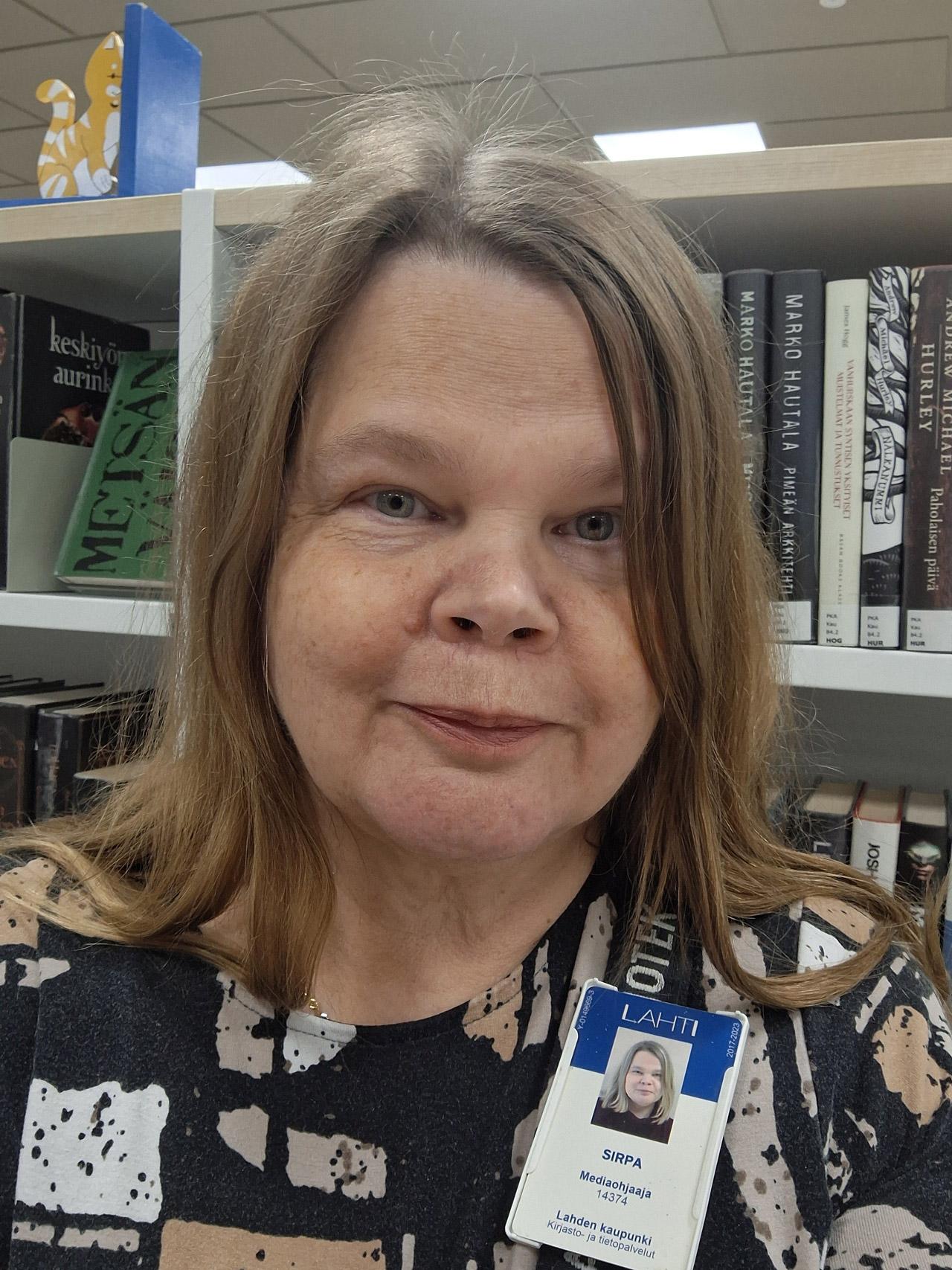 Kirjastotyöntekijä Sirpa Saareke katsoo kameraan taustallaan kirjahylly.