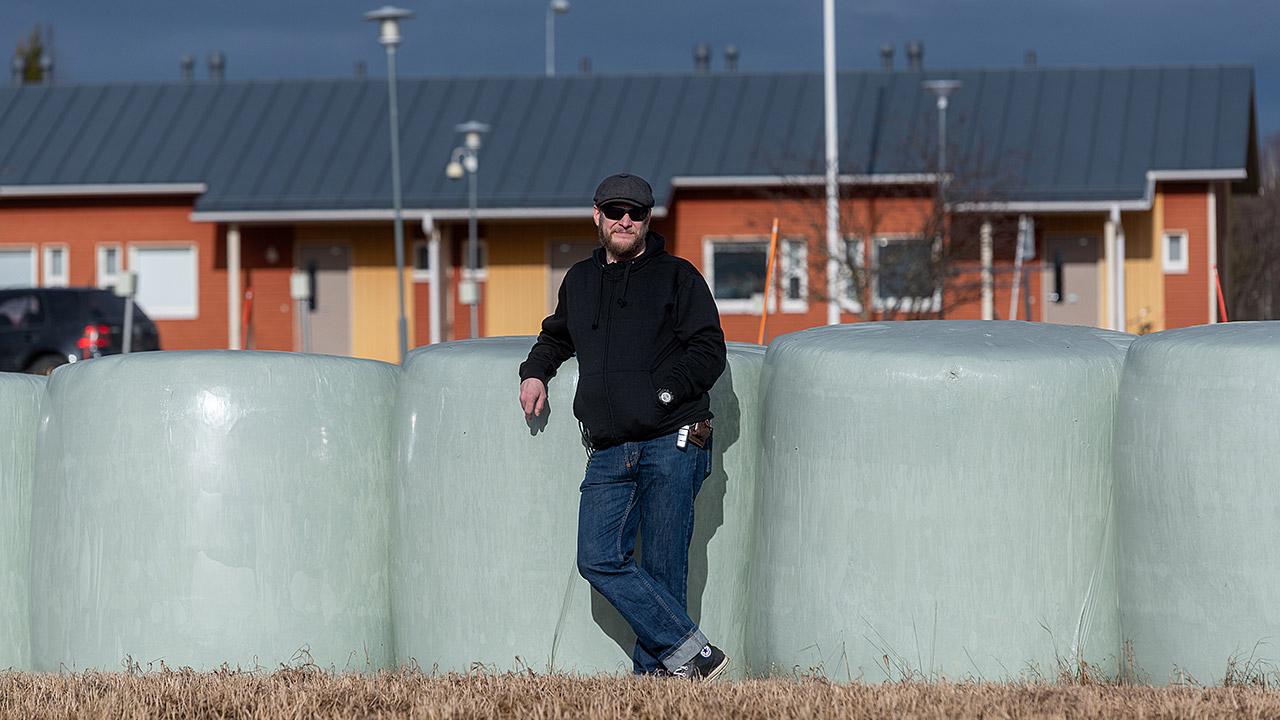 Asuntolaohjaaja Tommi Lapinjoki nojaa heinäpaaleihin.