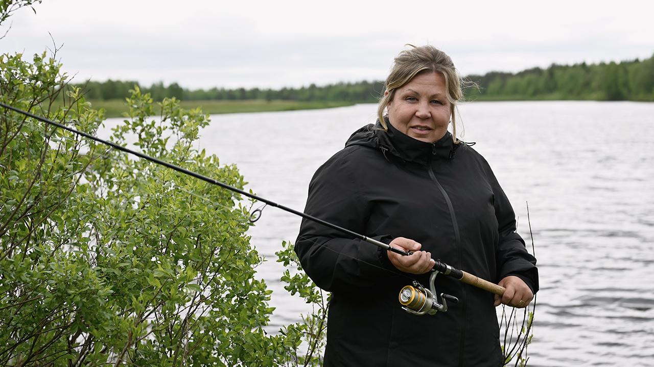 Perhetyöntekijä Terhi Tammela seisoo veden rannalla kädessään onki.