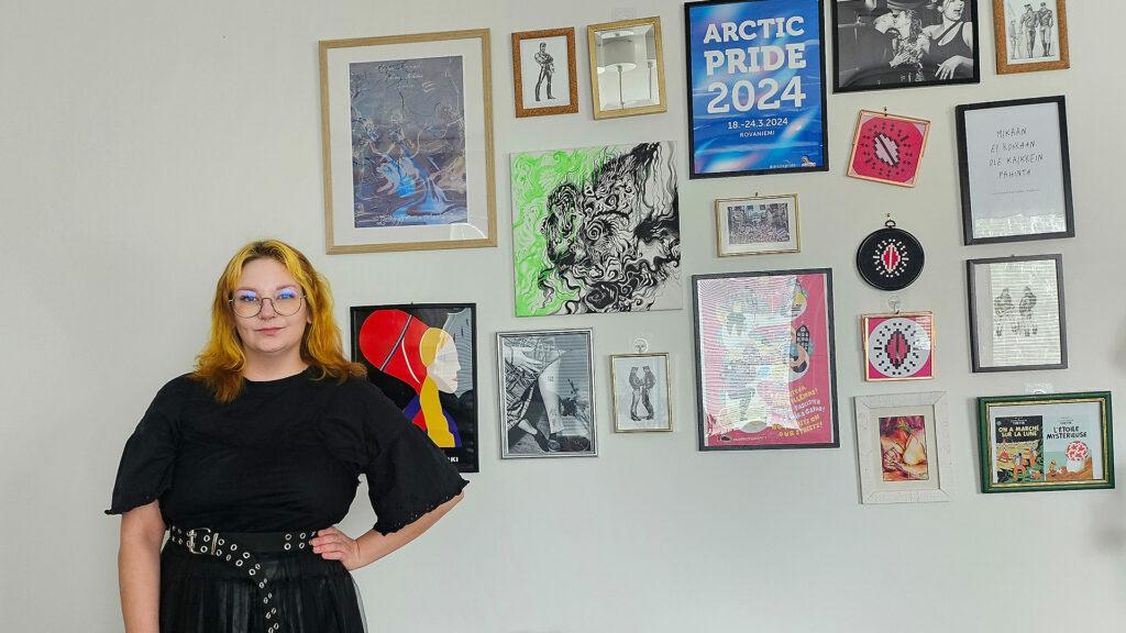 Mari Ikonen seisoo mustassa mekossa seinän edessä, jossa on yhdenvertaisuuteen viittaavia tauluja.