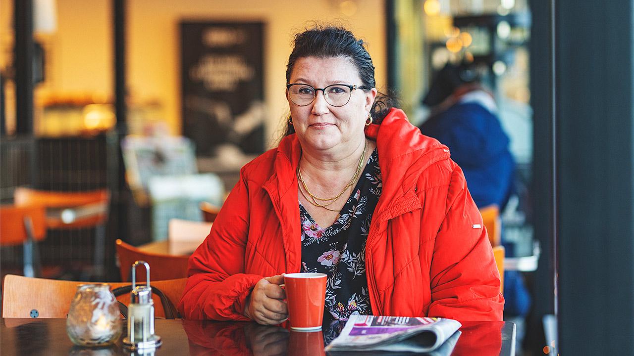 Työsuojeluvaltuutettu Päivi Virkkunen juo kahvia punaiseen takkiin pukeutuneena.