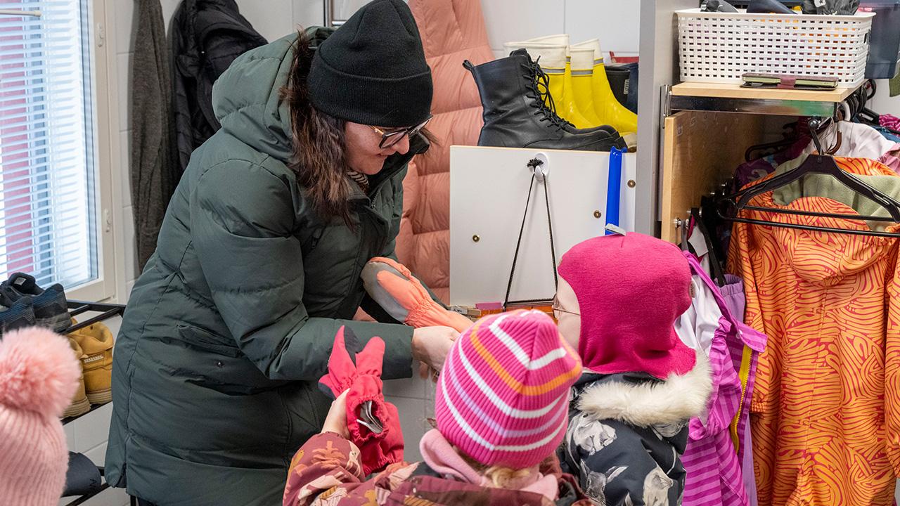 Varhaiskasvattaja keskustelee lasten kanssa päiväkodin aulassa.