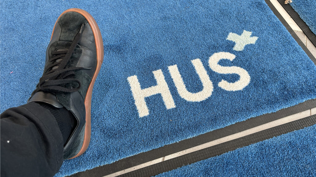 HUS-yhtymän logo kynnysmatossa, jolle astelee jalka.