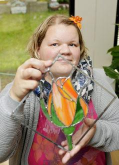 Tiina Stengård esittelee lasitaulua, jossa on oranssinvärinen tulppaanin nuppu.