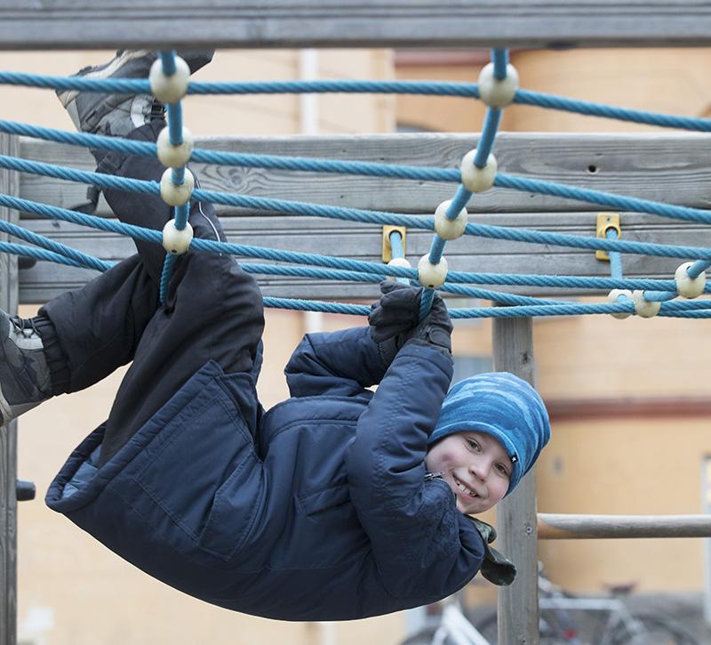 En pojke hänger med ryggen neråt i nätet i skolans klätterställning.