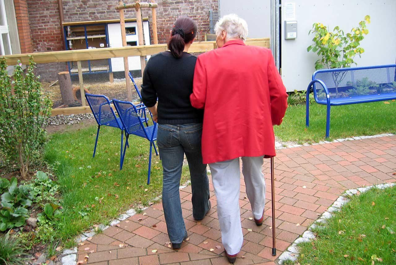 En äldre kvinna och en vårdare på promenad.
