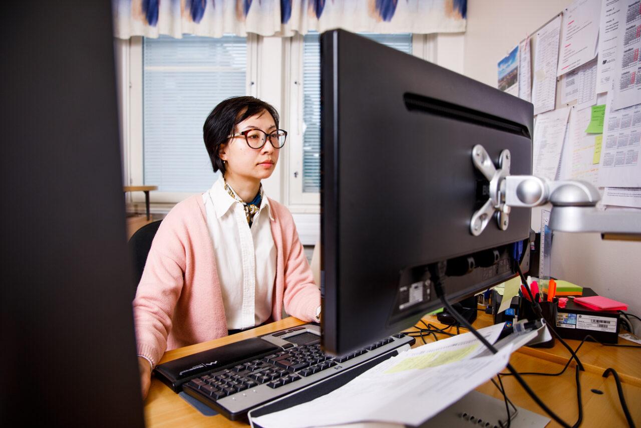 Jing Li sitter framför sina datorskärmar.