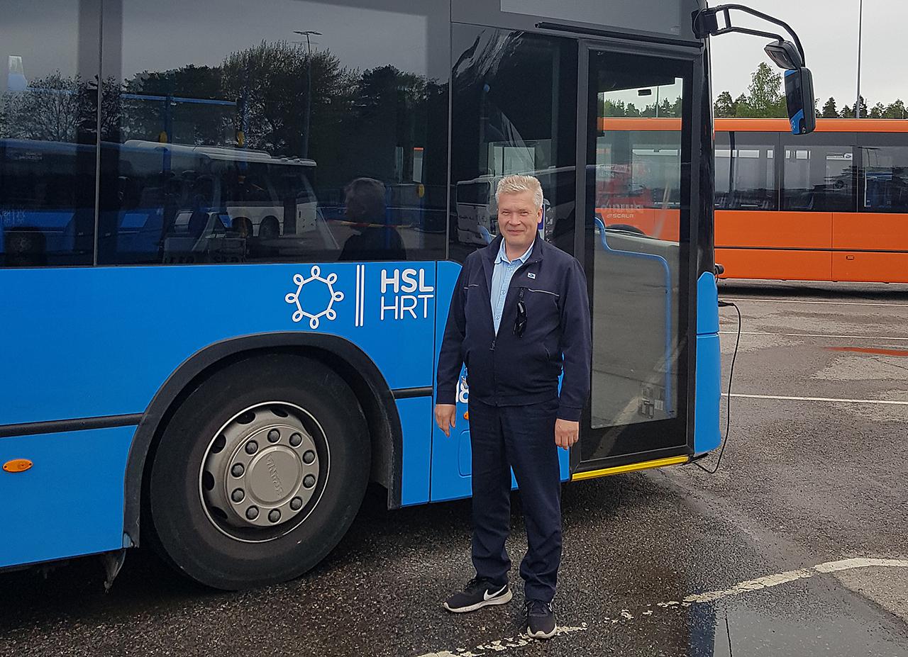 JHL:läinen linja-autonkuljettaja Lasse Laaksonen sinisen bussinsa ulkopuolella varikolla.