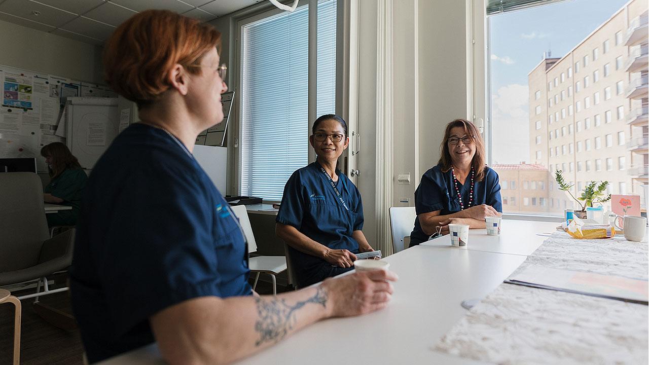 Laitoshuoltajat Maija-Liisa Lemmetti ja Yanchit Bupasopha juttelevat Lappeenrannan keskussairaalan kahviossa esihenkilönsä Minna Junnin kanssa.