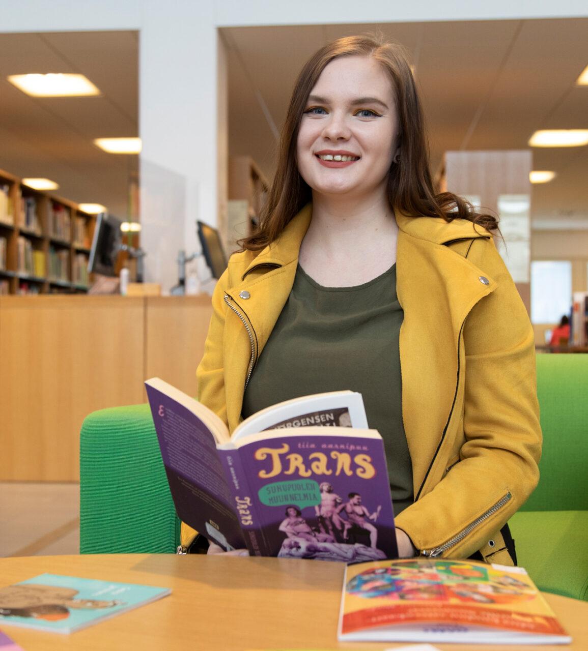 Opiskelija, Oulun Setan työntekijä Milla Heino istuu kirjastossa lukemassa trans-aiheista kirjaa.